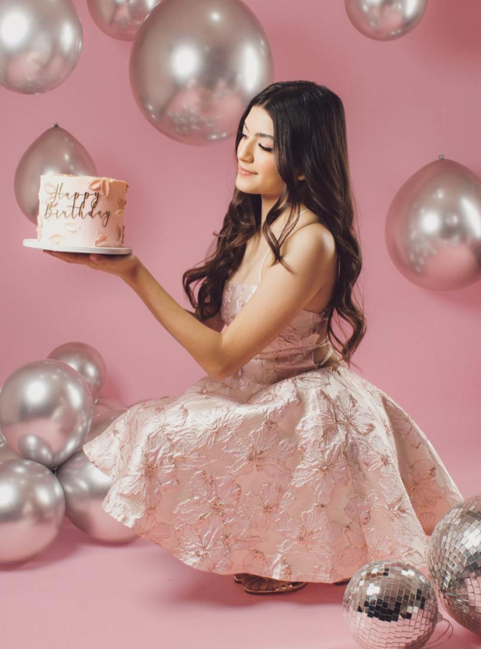 Sofía con vestido rosa satinado, sosteniendo su pastel entre globos plateados